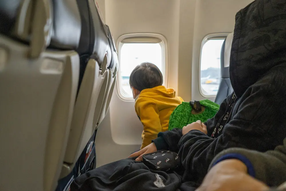 The kid is looking out of the window of an airplane during a long-haul flight to Asia