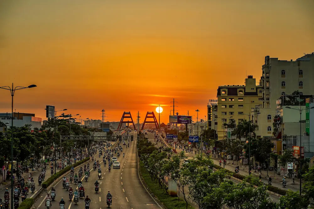 Busy street traffic in Ho Chi Minh City with millions of scooters as a family prepares to cross the road.